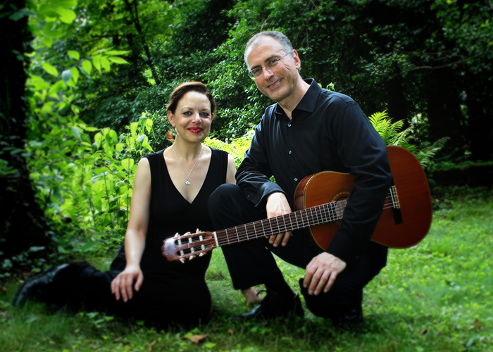 a woman and a man with a guitar stand in a grass field