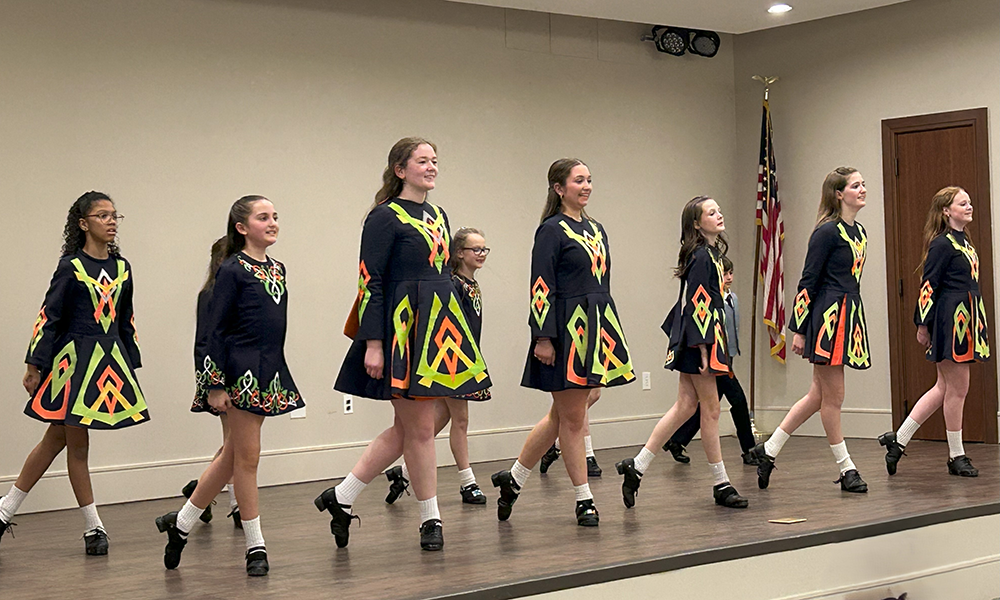 a group of young women in black, green, and orange dresses all dance on stage