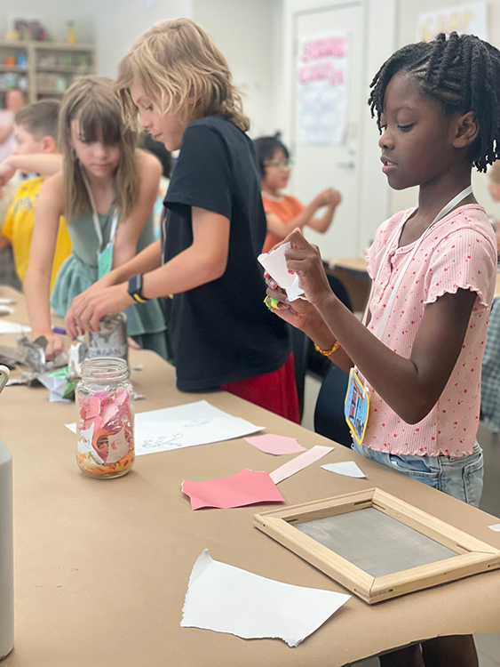 kids stand at a table as they make arts and crafts