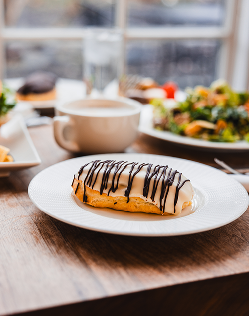 an eclair on a plate sits next to a full table of food