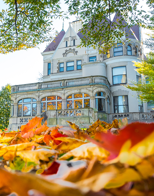 exterior view of a gilded age mansion, with colorful fall leaves in the foreground