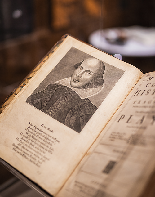 a portrait of shakespeare on an open page of a large book, sitting in a glass case