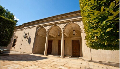 Exterior view of a stone building with pillared entrance and three doors