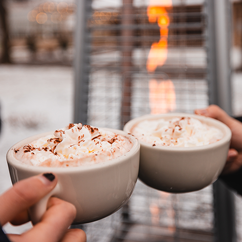 two mugs of hot chocolate held in front of a propane heater