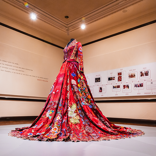 an ornately adorned red dress stands on a mannequin in a gallery space