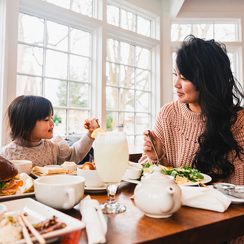 A woman and a young girl sit at a table eating food