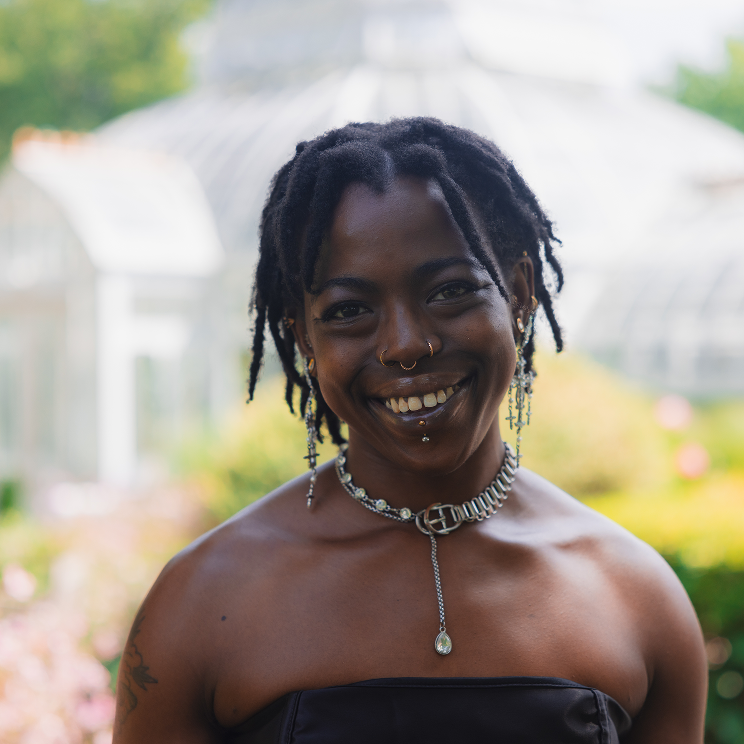 A headshot of a black person wearing a black top and a silver necklace