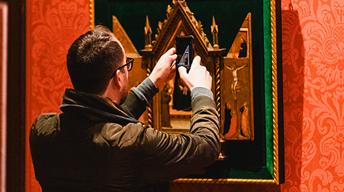 a person holds up a phone outside in front of a piece of art in a museum