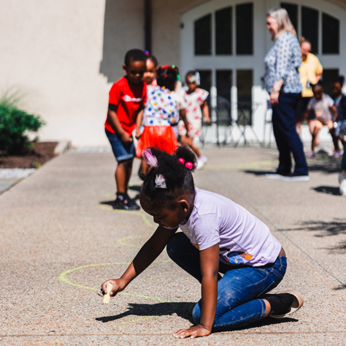 a young girl writes on a sidewalk with chalk