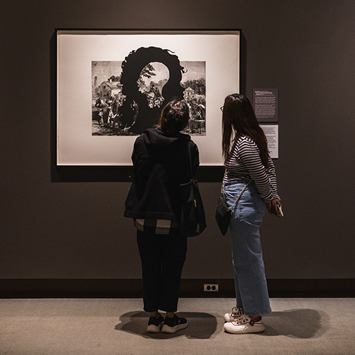 two people examine a large print hanging in a museum gallery