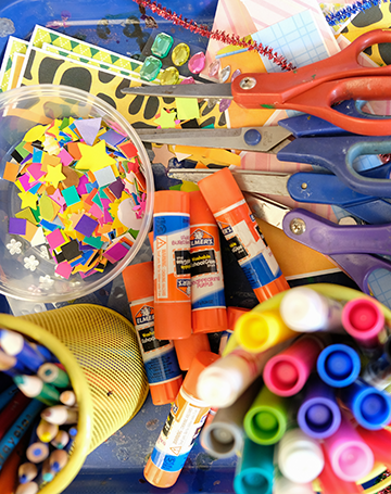 A table full of colorful art supplies, glue sticks, pencils, scissors, and more